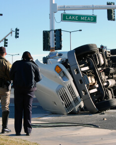people look at an overturned wrecked truck.